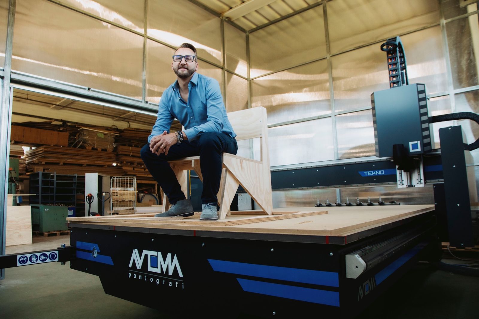 Angelo Cava sitting on a routed wooden chair on the TEKNO bed