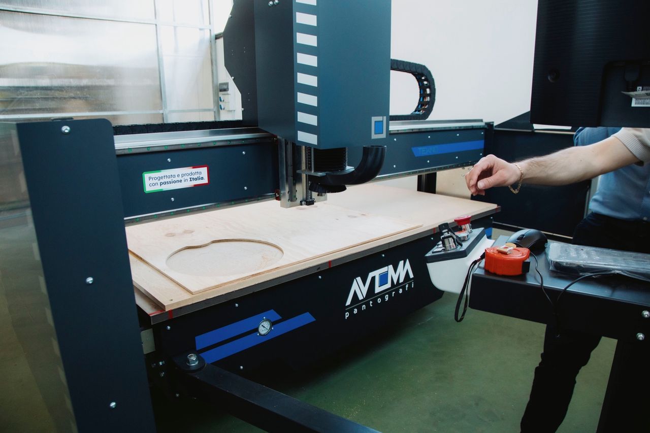 A routed workpiece on the TEKNO bed, with a hand at the console